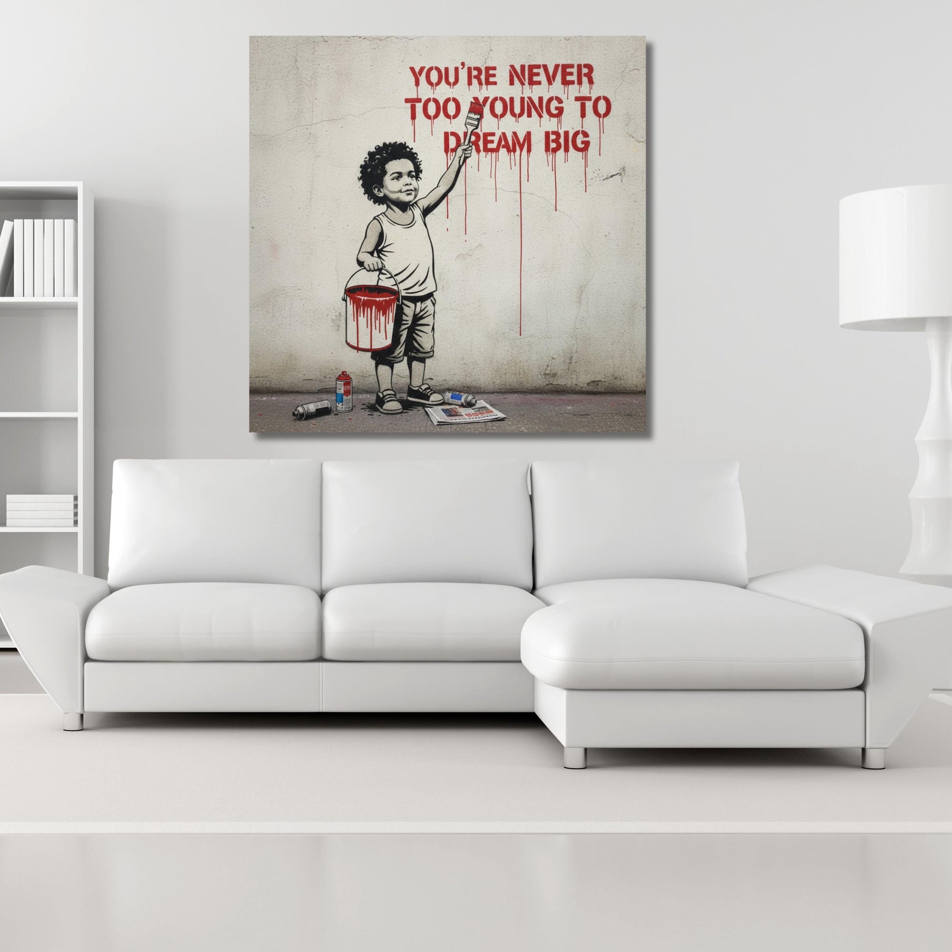 The image is a modern art piece featuring a young boy painting a wall with a bucket of paint. The text above the painting reads "YOU'RE NEVER TOO YOUNG TO DREAM BIG".